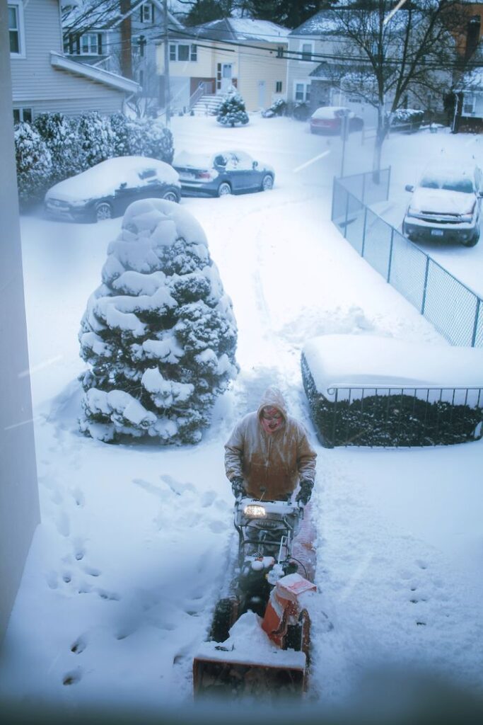 A person clears snow from a driveway with a snowblower in a residential area during winter.
